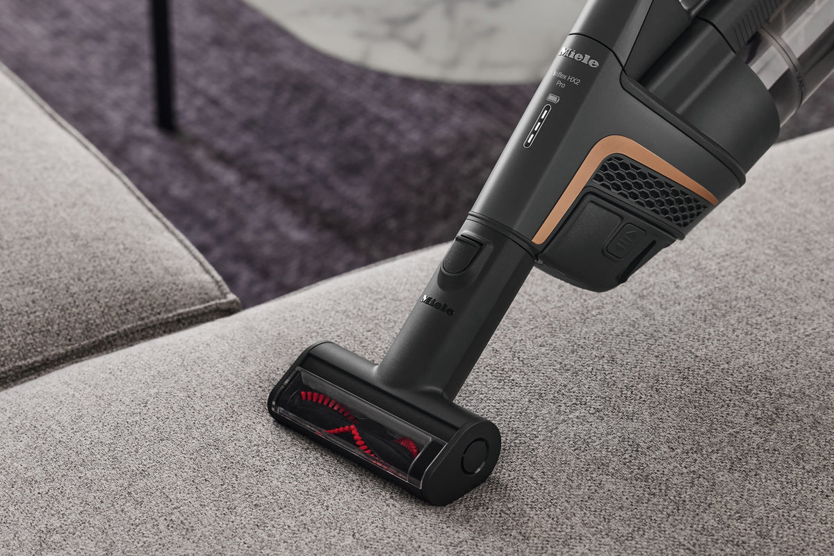 Miele HX-EC 10 Compact Handheld Brush — shown cleaning a sofa cushion