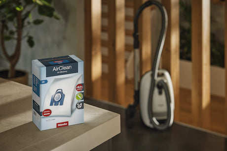 Miele AirClean filter packaging on a wooden surface with a vacuum cleaner in the background.