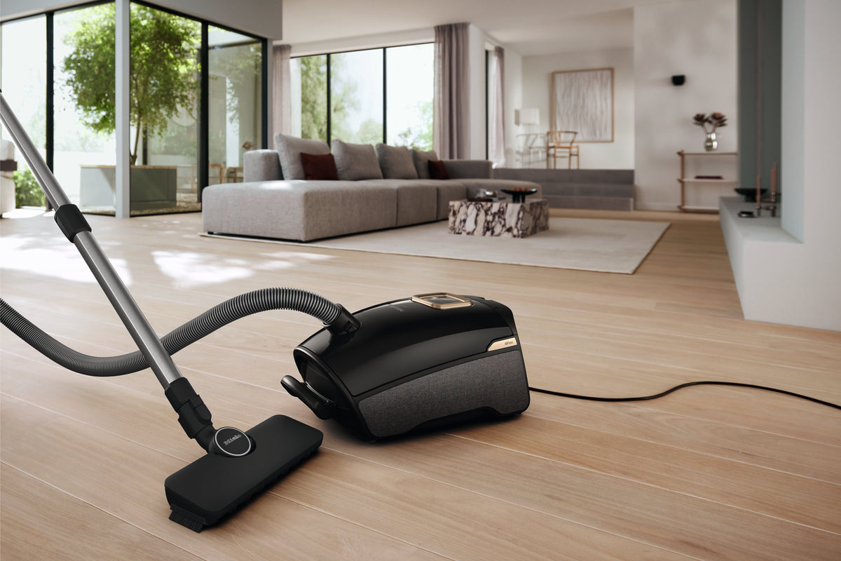 Miele Guard L1 AllFloor canister vacuum beside a rug in a bright living room