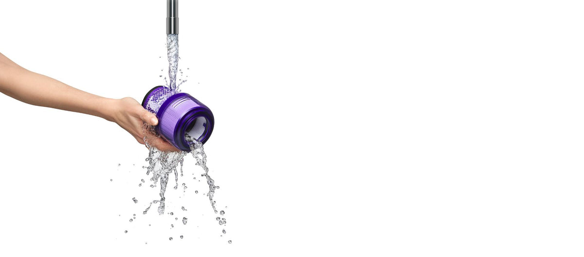 A hand rinses a removed Dyson cordless vacuum filter under running water